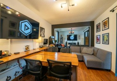 Large meeting area with wooden tables, grey sectional sofa, and wall-mounted screens.
