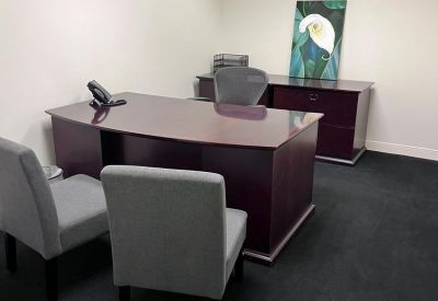 Private office with a dark wood desk and two grey guest chairs.