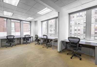 Open-plan office space with multiple desks situated along large windows.