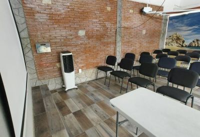 Seminar room with rows of black chairs, a white table, and an exposed brick wall.