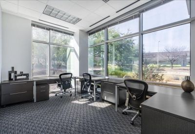Bright corner office with three workstations and large windows overlooking trees.