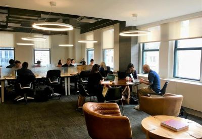 Modern coworking area with long communal tables, ergonomic chairs, and circular pendant lighting.
