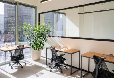Bright office space with wooden desks and city views through large windows.