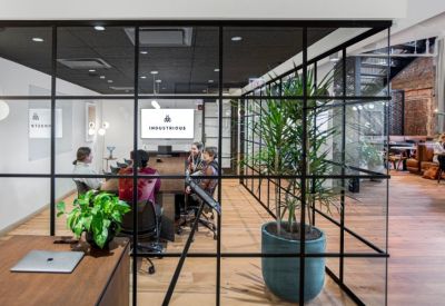 Glass-walled meeting room with people seated around a table and the company logo on screen.