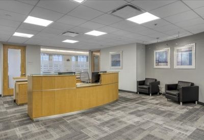 Modern reception area with a curved wooden desk and comfortable black leather armchairs.