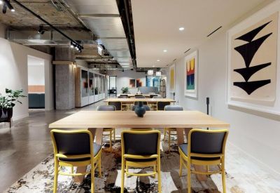 Bright coworking lounge with wooden tables, yellow-framed chairs, and abstract wall art.