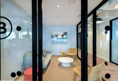 A modern lounge area with a light blue sofa, colorful side tables, and wooden chairs.