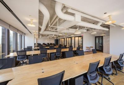 Large open-plan coworking space with long wooden desks and ergonomic black chairs.
