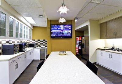 Communal kitchen area with a long white breakfast bar and a wall-mounted television.