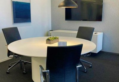 Modern meeting room with a round white table, blue artwork, and black pendant lights.
