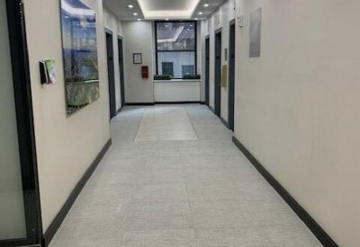 Long office corridor with light grey tiling and recessed ceiling lighting.