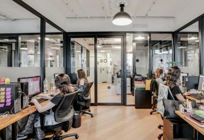 Glass-walled office space with several workstations, ergonomic chairs, and natural light.