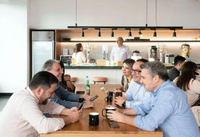 Lively communal dining area with people sitting at a long wooden table and an open bar in the background.