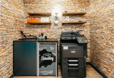 Office utility area with stone-textured walls featuring a professional printer and shredding station.