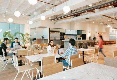 Open-concept dining and coworking space with white tables, wooden chairs, and globe pendant lights.