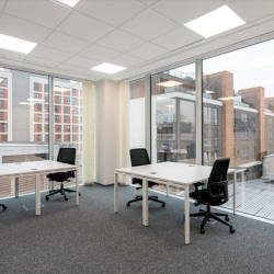 Clean four-person office suite featuring white desks and large windows with urban views.