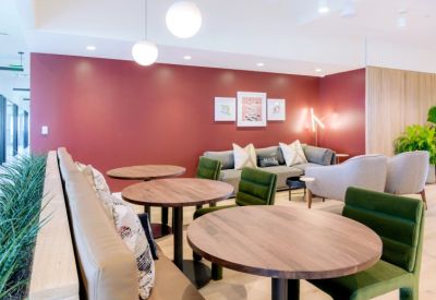 Colorful lounge area with circular tables, green velvet chairs, and a red feature wall.