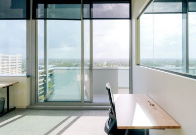 Bright private office with a wooden desk and sliding glass doors leading to a balcony.