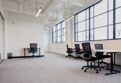 Bright open-plan workspace featuring several black mesh chairs and minimalist wooden desks.