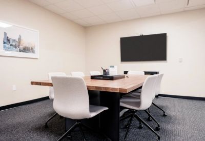 Professional conference room with a large wooden table, white chairs, and a wall-mounted screen.