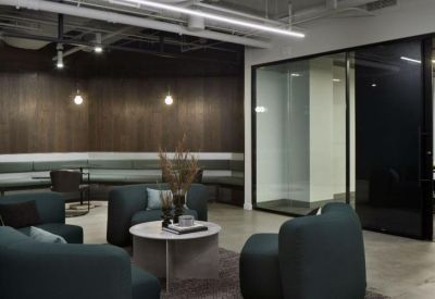 Contemporary lounge area featuring teal armchairs, a marble coffee table, and glass-walled meeting rooms.