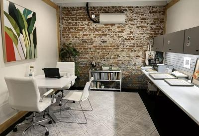 Private office featuring a brick accent wall, white desks, and vibrant botanical wall art.