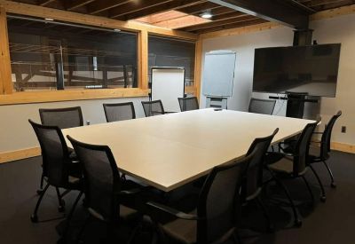 Professional conference room with a large white table, mesh chairs, and a wall-mounted TV.