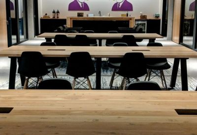 Sleek coworking lounge with wooden communal tables and modern graphic wall art.