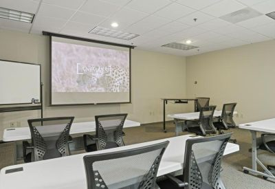 Spacious meeting room with projector screen and rows of training tables.