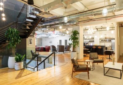 Spacious communal lounge with a grand staircase, wooden floors, and potted plants.