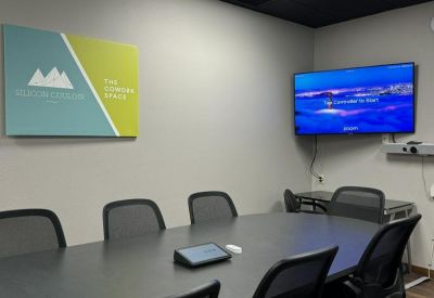 Modern conference room with a large screen, grey table, and ergonomic mesh chairs.