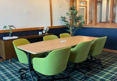 Boardroom with a light wood table, green chairs, and green tartan carpeting under timber ceilings.