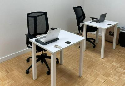 Private office workspace with two white desks, black chairs, and light wood flooring.