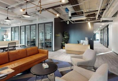 Modern reception lobby with leather sofa, grey armchairs, and wood-paneled desk.