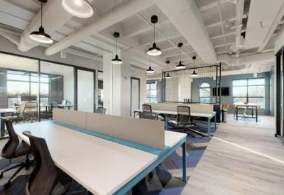 Open-plan office space with long white desks, ergonomic chairs, and industrial ceilings.