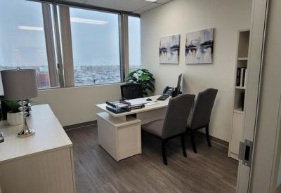 Private office with large windows, a white desk, and grey guest chairs.