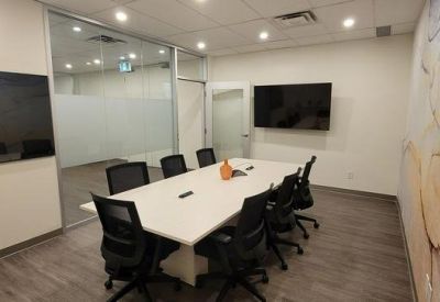Spacious boardroom with large white table and wall-mounted monitor.