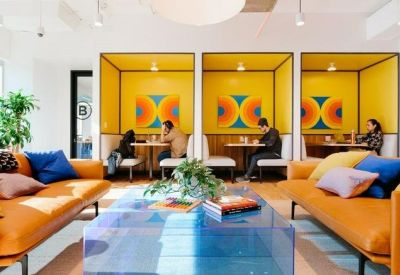 Communal lounge with orange sofas, blue cushions, and yellow private meeting booths.
