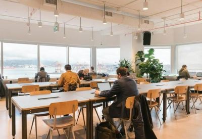 Coworking office area with long rows of wooden desks and large windows overlooking the city.
