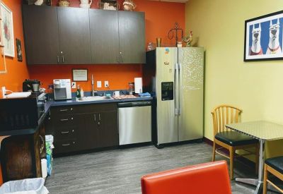 Communal kitchen area with orange walls, dark cabinetry, and a small dining table.
