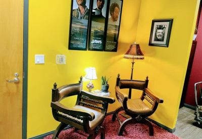 Small seating area with two ornate wooden chairs and a pink shag rug against a yellow wall.