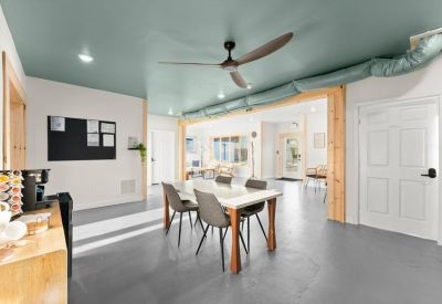 Communal dining area with a wood-accented doorway, ceiling fan, and white dining table.