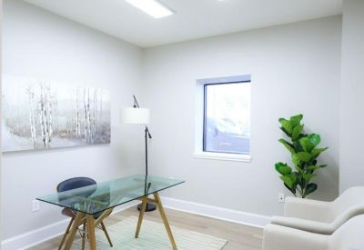 Bright private office with a glass desk, stylish rug, and natural light from a window.