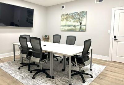 Modern conference room with a white table, mesh chairs, and wall-mounted TV.