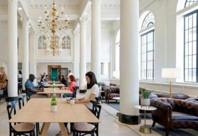 Grand communal lounge with high ceilings, white pillars, gold chandeliers, and leather seating.