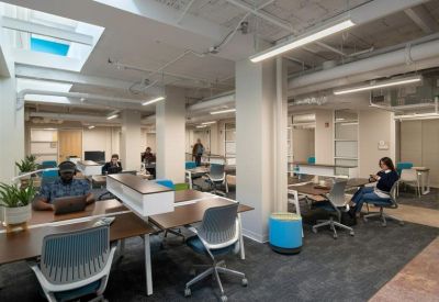 Open-plan coworking space with modern desks, blue accent seating, and bright skylights.