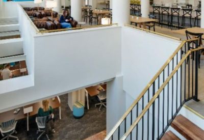 Bi-level lounge and workspace area connected by a wooden staircase with gold-toned railings.