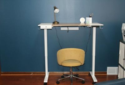 Modern height-adjustable standing desk with a yellow office chair against a blue wall.