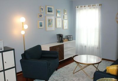 Lounge area featuring a blue armchair, white sideboard, and a gallery wall of framed art.