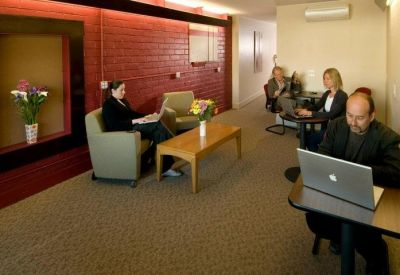 Modern breakout area with people working on laptops in comfortable armchairs against a red wall.